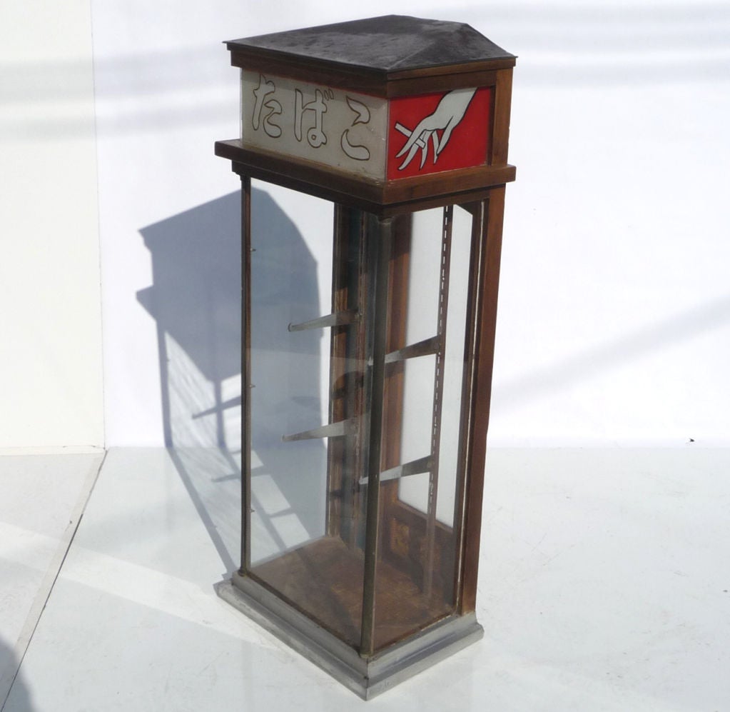 Loaded with charm, this tall glass cabinet most likely stood in a Japanese market or cafe to sell tobacco products. The roof is tin and the cabinet is a combination of oak, glass, and aluminum. Three hand painted panels adorn the upper portion,