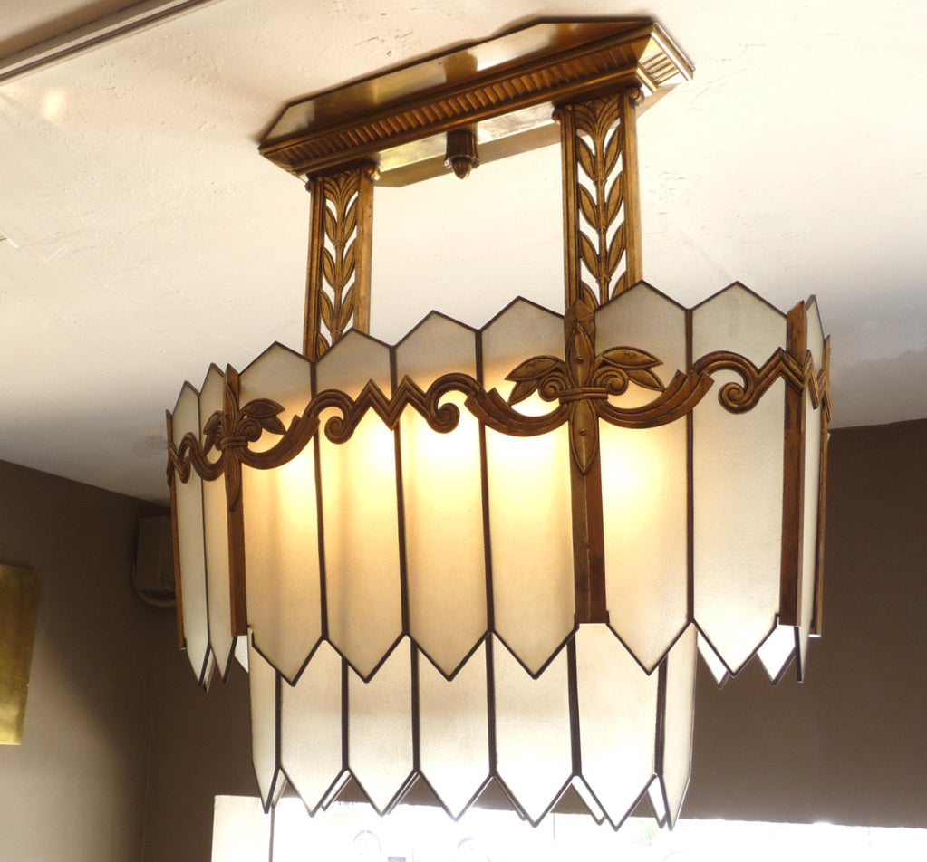 This fantastic chandelier has a great pedigree, and an amazing presence. Panels of textured glass taper inward, surrounding an octagon shaped bottom panel. The glass panels are surrounded with incredibly stylized gilded metalwork. The ceiling panel