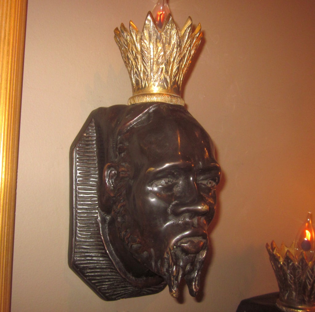 These wonderfully stylized sconces depict a bearded king with golden crown. The castings display a warm, dark patina and are without any condition issues. A single candelabra socket is housed within the crown. We have chosen flickering flames for