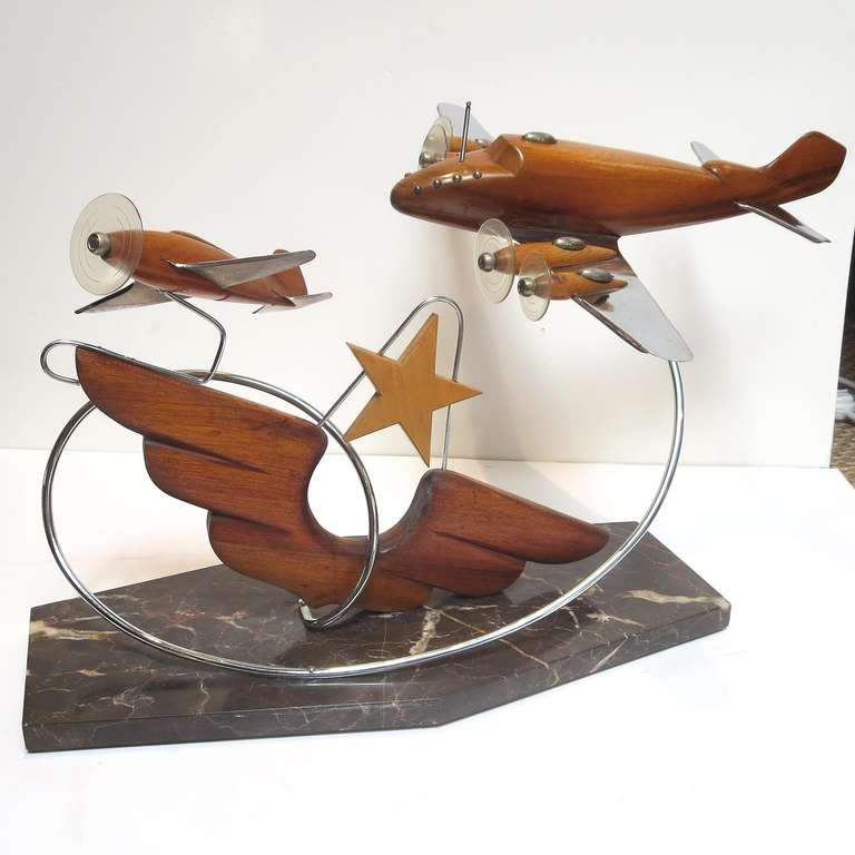 Mounted over a black marble base, this great pair of planes seem to soar in tandem flight. Bodies are sculpted and polished mahogany, with wings of chromed steel. Original clear plastic discs are intact, simulating spinning propellors. We have seen