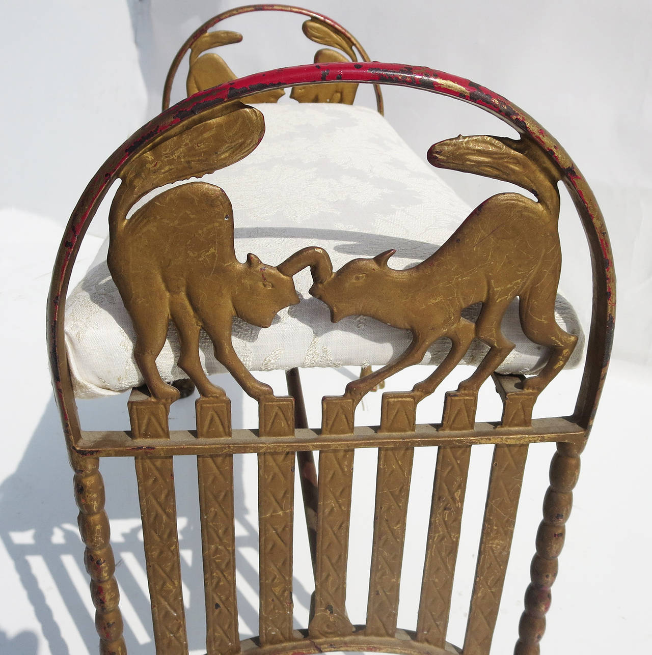 This ultra-charming iron bench is decorated in an alley cat motif. Featuring two cats at each end, they are perched on a fence and starting to scrap. One cat has a paw up, aimed at the opposing cats head. Even the four feet of the bench are feline