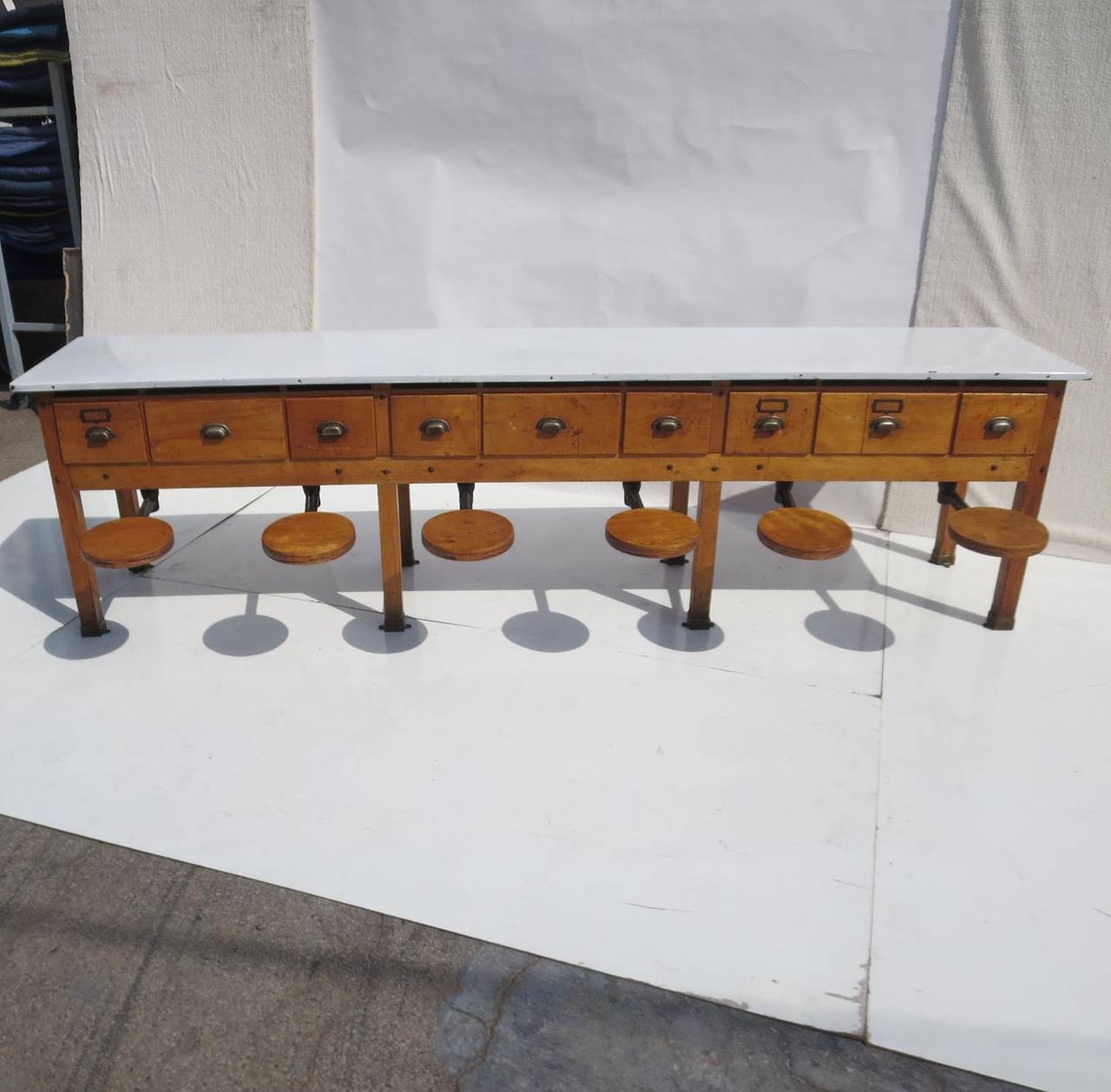 This fantastic table was utilized in a factory or laboratory, where workers could sit side by side. When not being used, the seats swing underneath the table and out of sight. The top is porcelain enameled steel, and the wood is an original finished