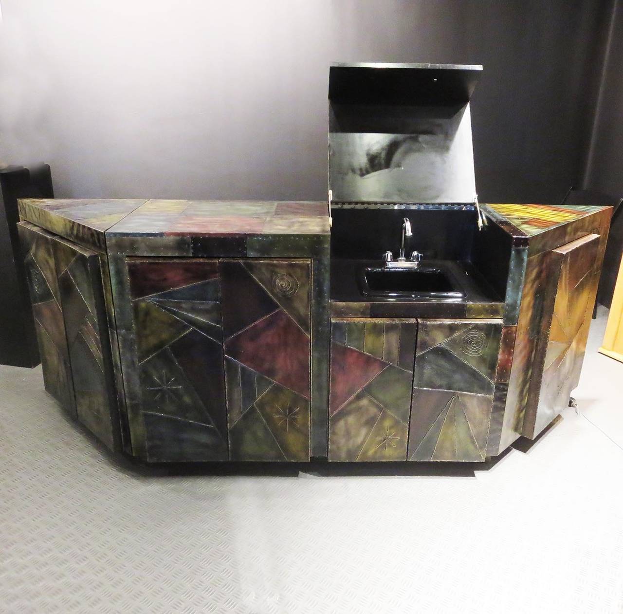 Custom bar with patchwork polychrome finish and riveted and welded decoration consisting of three base units, one with integrated wet sink and cabinetry. All surfaces, including the back wall, are surfaced with multicolored steel panels in a