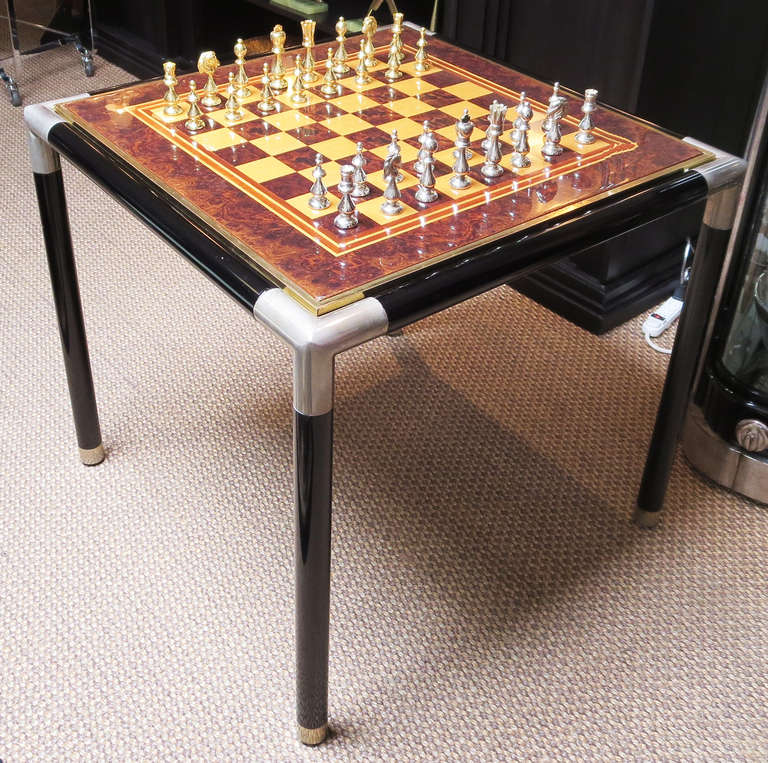 This lovely game table is of the finest design and materials. The featured inlaid top is a combination of blonde oak, dark burled wood, and border stripes of red and blonde mahogany. The table is a combination of lacquered wood and polished nickel