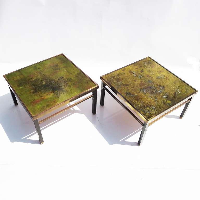 This lovely pair echo the works of Philip and Kelvin Laverne, who produced similar versions of historical themed tables in the 1960's. Ours are reverse painted and gold leafed under glass. The edges and legs are a darkened brass or bronze, and