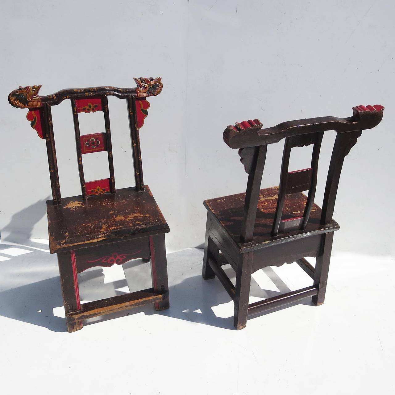 This great pair display a wonderful patina of age, and exude a fantastic charm. Both chairs feature carved dragon heads on the top corners, and various painted decorative elements. They are lovingly worn, but solid and comfortable.