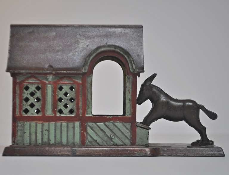This wonderful mechanical bank was patented in 1880 and retains beautiful original paint. One places a coin between the rear legs of the donkey. By pushing the small button the donkey bucks upward, flinging the coin into the barn. At the same time,