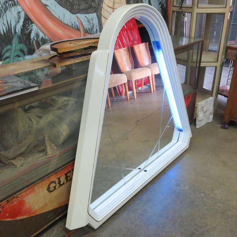 This stylized pyramid mirror is surrounded by a wide lacquered wooden frame which encompasses two side lights. The mirror is etched with a pleasing linear design, and is in excellent condition. A center button activates the lighting, and wall