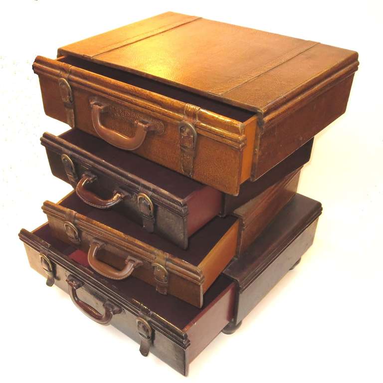 A wonderful and whimsical design, this side table sized cabinets resembles a precarious stack of briefcases. The surfaces are textured and colored vellum, with leather strap trim. All are supported by four wooden ball feet. Created by an unknown