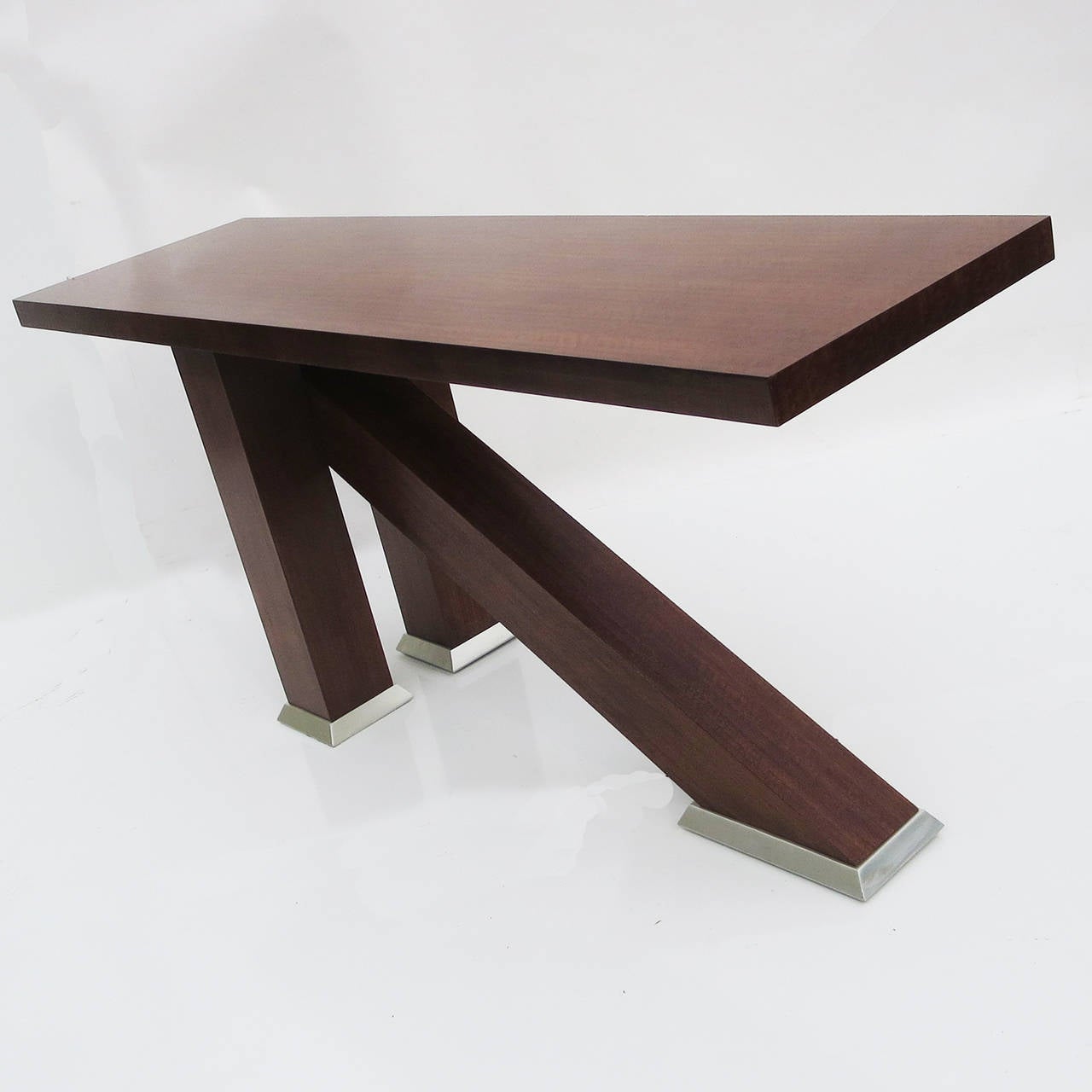A great design by an unknown designer. The tabletop floats over three intersecting legs, and is very solid in form and construction. The wood appears to be a satinwood, with a darker walnut stain. The legs are capped by satin silvered metal feet, to