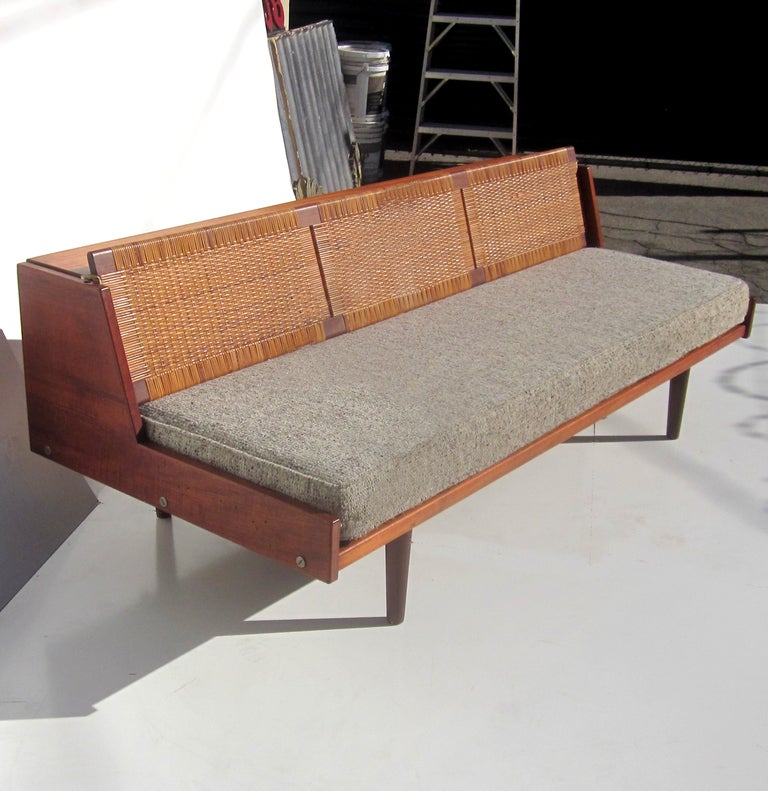 Created in teak wood with a cane back, this classic Wegner sofa converts to a sleeping bet by simply lifting up the back. Once raised, the back exposes a deeper cushion, roughly the size of a twin bed. The wood is all original and in very nice