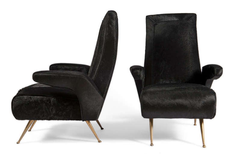 Club chairs with cantilevered arm on brass splayed feet. Upholstered in ebony hair on hide with double meiter stitch detail.