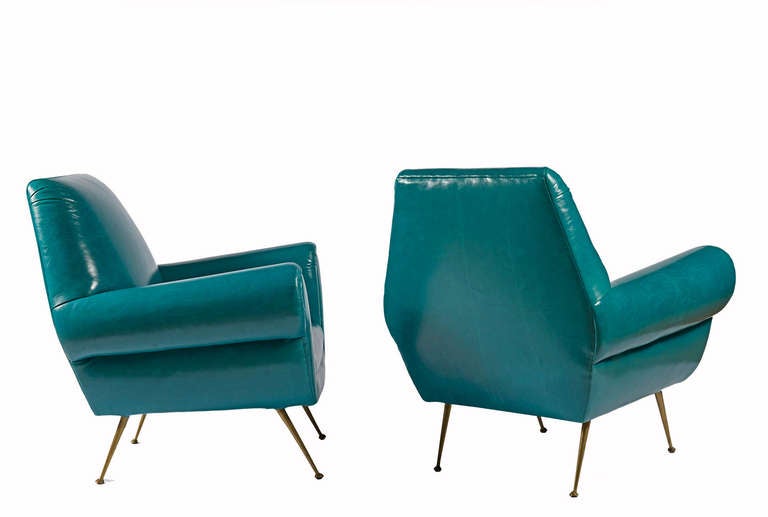 Club chairs in the manner of Marco Zanuzo, upholstered in peacock blue leather with a tight seat and back on splayed brass legs.