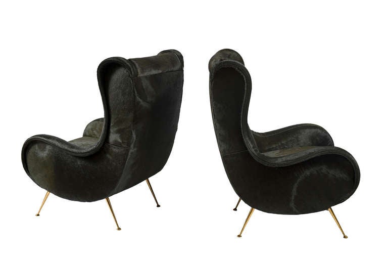 Club chairs in the manner of Marco Zanuzo, upholstered in ‘INK’ hair on hide, resting on brass canted legs.