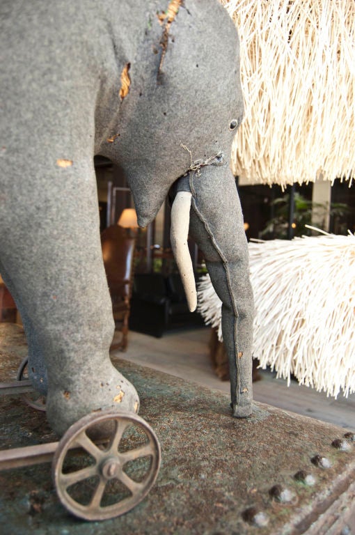Rare Steiff riding elephant made of rush wrapped in dark grey felt with signature brass grommet on top right side of elephant on metal wheels, with natural wear and tear, missing right side ear and left side tusk and tail.