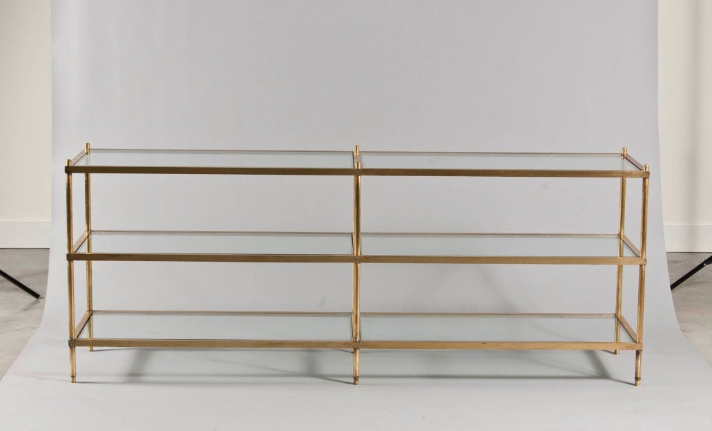 Open frame shelving unit with six inset glass tops resting on polished brass frame.