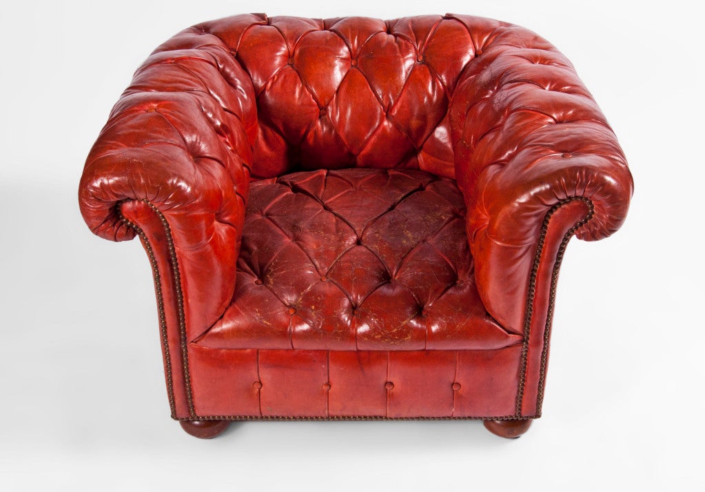 Pair of red leather Chesterfields, tufted back, arms, seat on wooden bun feet with scrolled arms and nailhead trim. Originally orange, aged to red.
