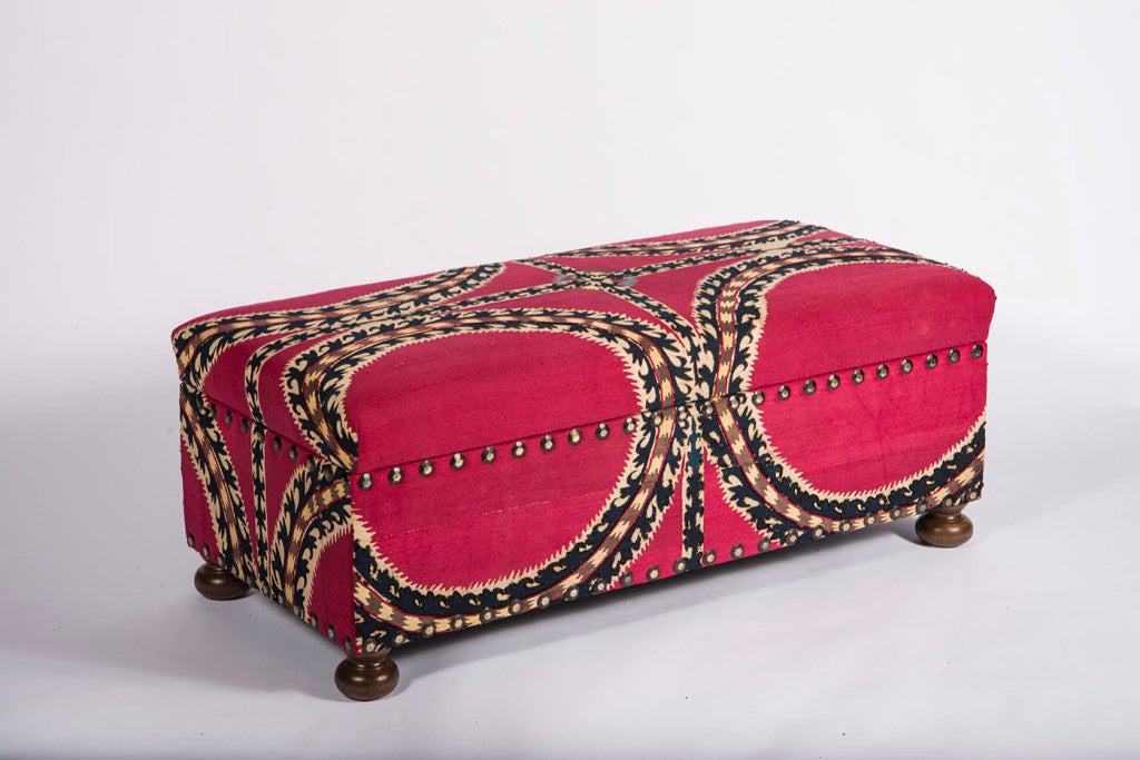 Vintage suzani fabric in original rich pomegranate dye upholstered on wooden lift-top frame with brass nailheads resting on bun feet.
