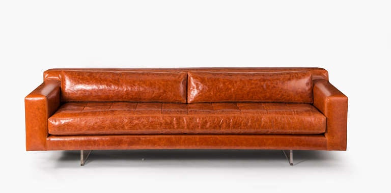 Modern rectangular sofa upholstered in burnt orange leater with seat cushion and rectangular two back pillows on two lucite legs.