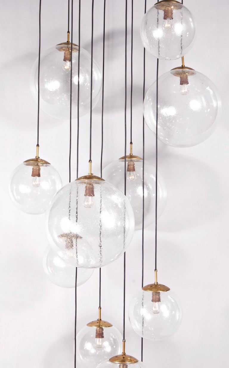 Cascading blown glass orbs of various diameters with brass caps hanging from extruding brass arms attached to center conical brass canopy.