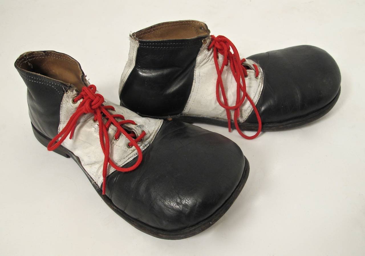 A large pair of black and white leather clown shoes. From heel to toe measure 14 inches.