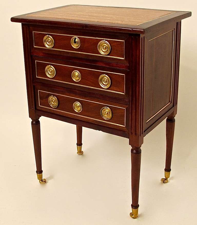 Mahogany bedside chest of drawers with inset marble top, brass moldings around recessed side panels and drawer fronts flanked by fluted pilasters on turned legs ending in brass castors, French, circa 1870.