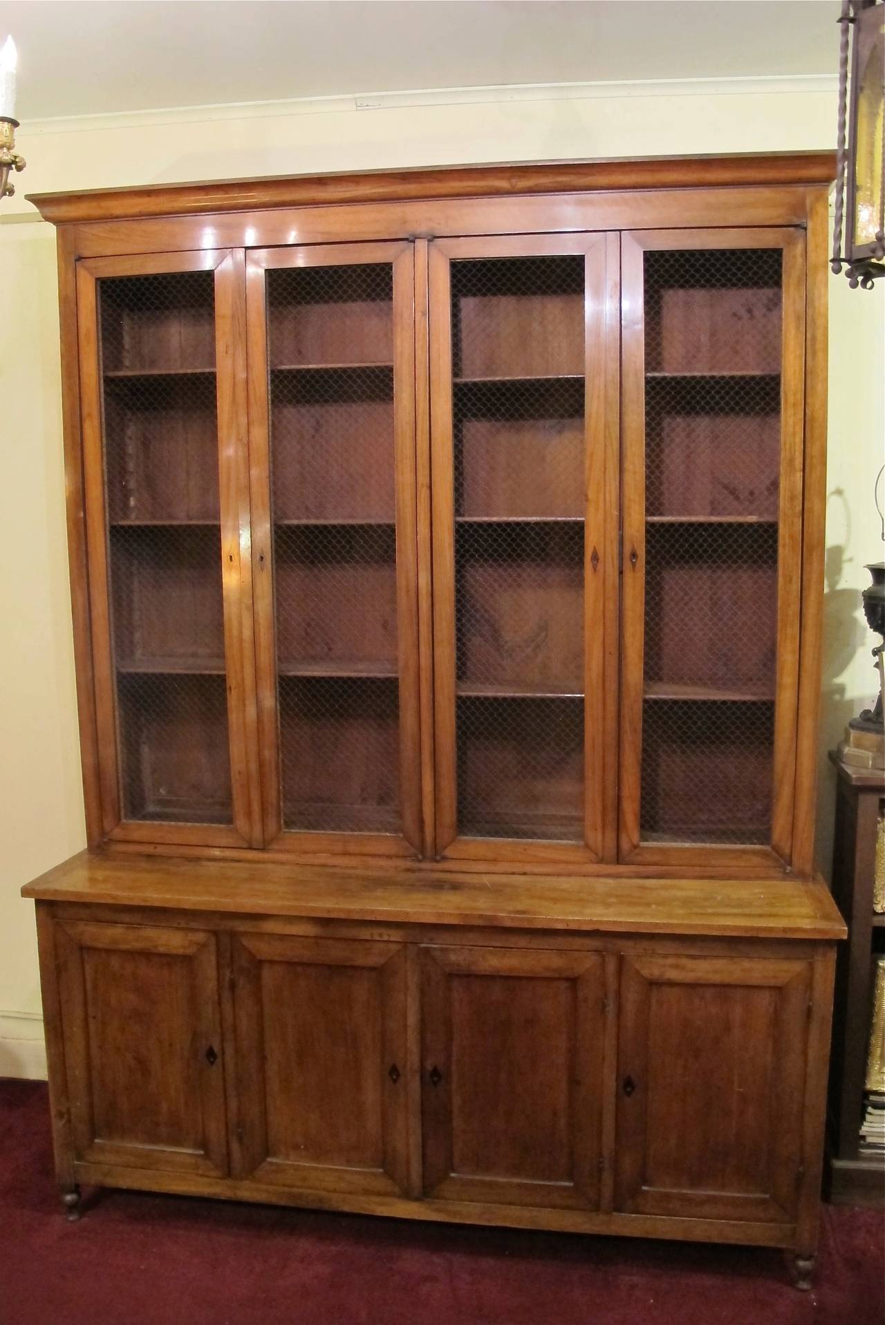 Directoire Caucasian wingnut (walnut) bookcase. Upper section with pair of double doors with brass wire mesh and three adjustable shelves. The lower section with a pair of recessed panel doors in the center flanked by single door cabinets. All doors