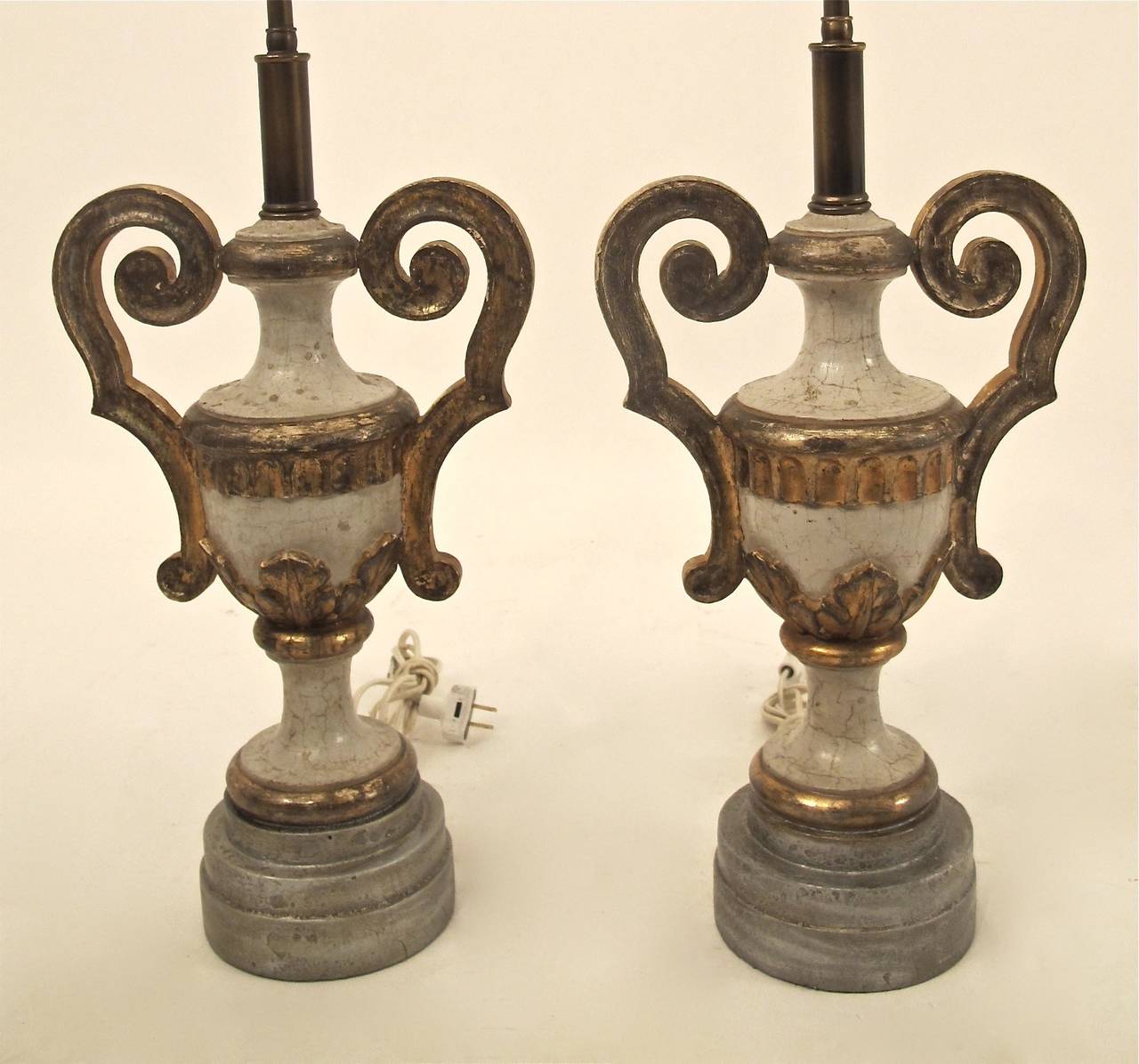 A pair of carved wood, painted and parcel-gilt urns converted to lamps. Very pale blue paint with parcel silver and gold gilt detail on silver leaf custom-made bases. Recently re-wired. Shades not included.