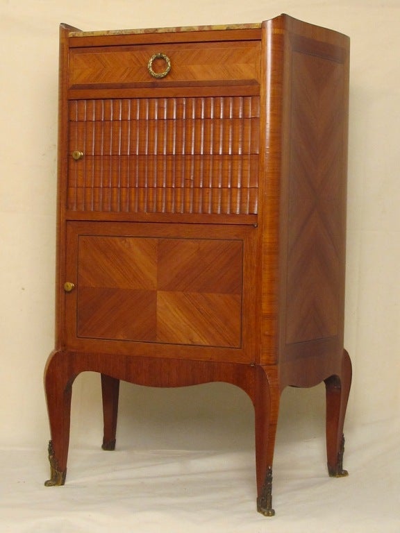 A beautifully handcrafted small side cabinet table of tulip wood and mahogany with a tambour sliding middle door, lower cabinet and top single drawer and having its original marble top, France, early 20th century.