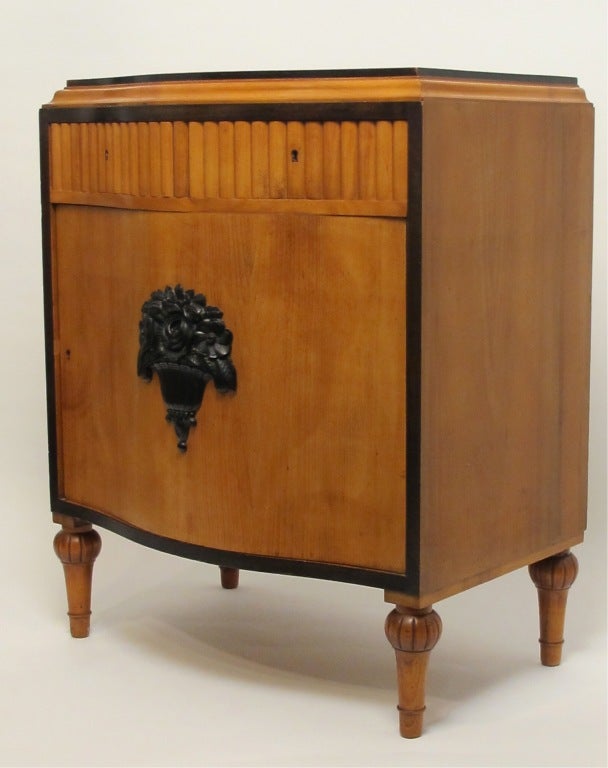 Wonderful Art Deco cabinet with two ribbed drawers above single door with a single shelf inside. Hand Carved Black Lacquered Basket of flowers appliqued to the door front.  Standing on bulbous turned legs.  European, Circa 1930.  This would make an