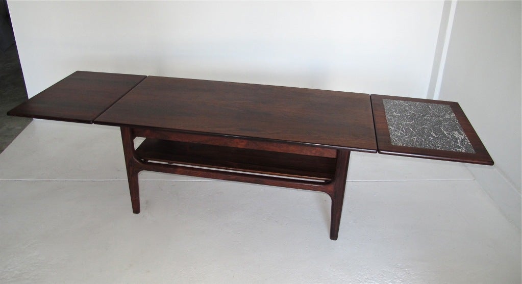 A mid 20th century Danish modern solid rosewood coffee table with extending leaves on each end. Each leaf extends 15.25 inches, one leaf having an inset faux marble top, marked Made in Denmark. Recently refinished, and in beautiful condition.