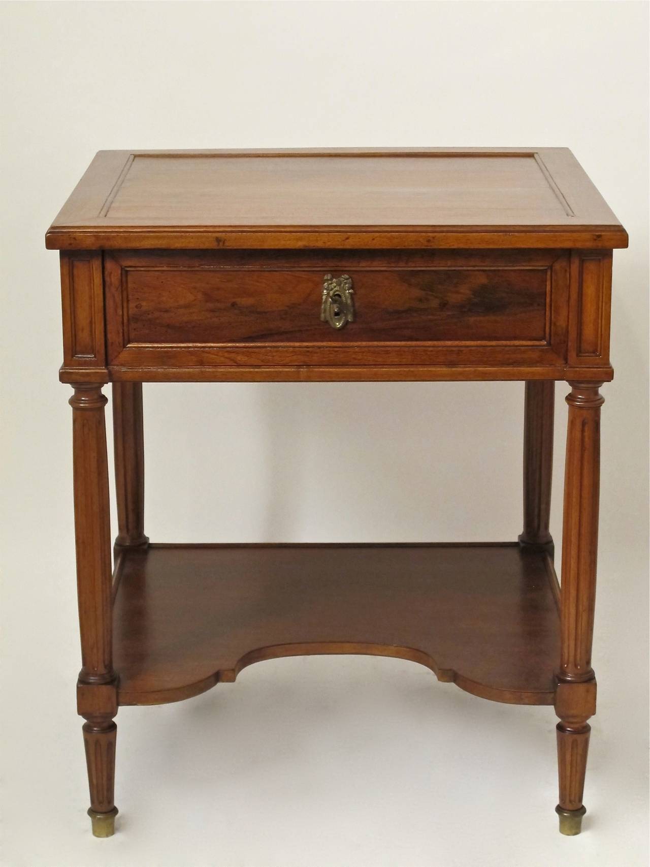 A 19th century Louis XVI style side/bedside table with a recessed panel top above a single drawer (with key) and tapering fluted legs ending in brass sabots. Quality bench made walnut table with very nice detailing on all four sides.