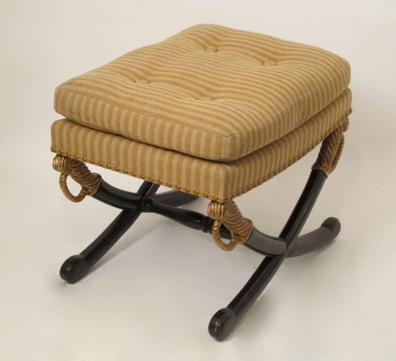 Ebonized saber leg ottoman or stool with gilt handles supporting the upholstered seat with button tufting. Has original old metal bracing on the legs, paint and gilding redone in the 20th century, seat cushion is down, upholstery is vintage and