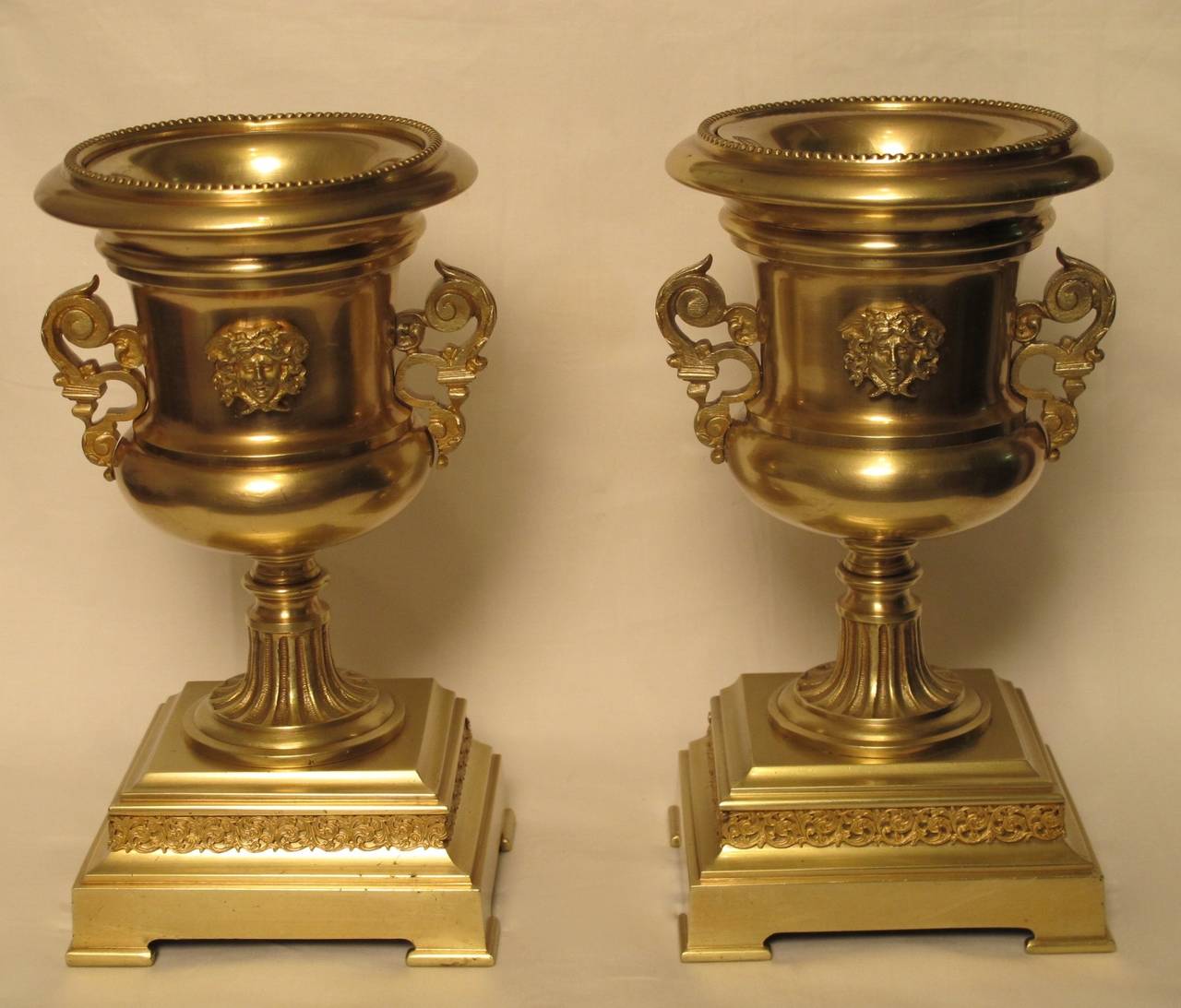 A pair of champagne urn shaped brass potpourri garnitures with mask faces in relief on stepped plinth bases. France, circa 1840.