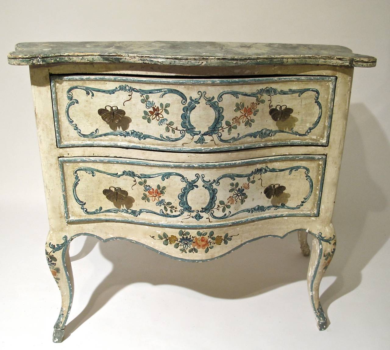 Charming and shapely Genoese painted commode. Shaped greenish blue and black faux marble top above white painted two-drawer commode. Blue C scroll panels painted on the drawer fronts with vining pink and blue flowers and brass butterfly pulls. The