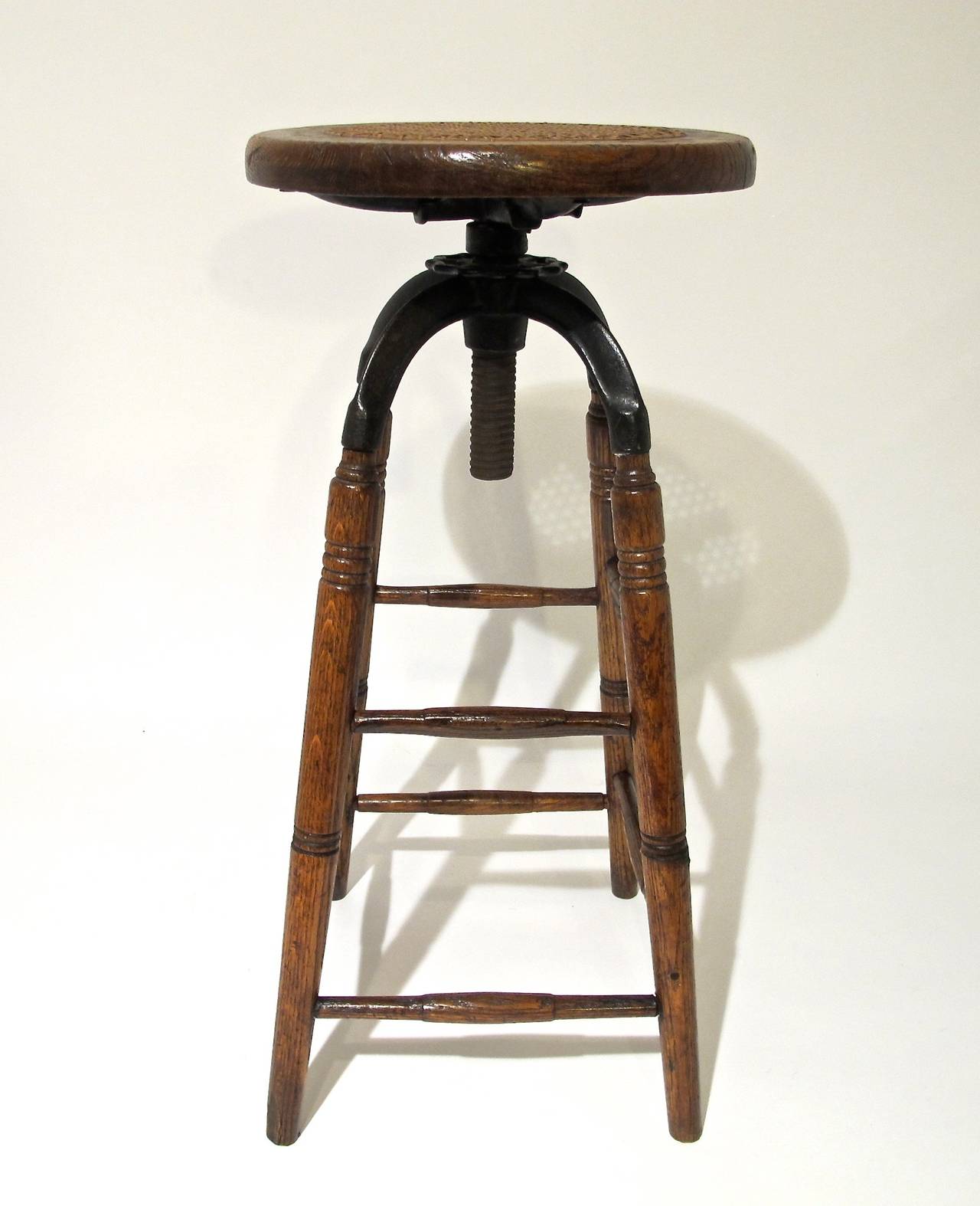 Swivel Cane Seat Stool with Iron supports and height adjuster on four oak legs and double rungs on all four sides.  American, Late 19th. Early 20th. Century.