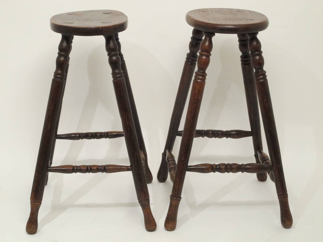 A slightly unmatched (one seat is a bit more oval than the other) pair of elm and yew wood pub stools with turned flared legs and turned dowel supports.
