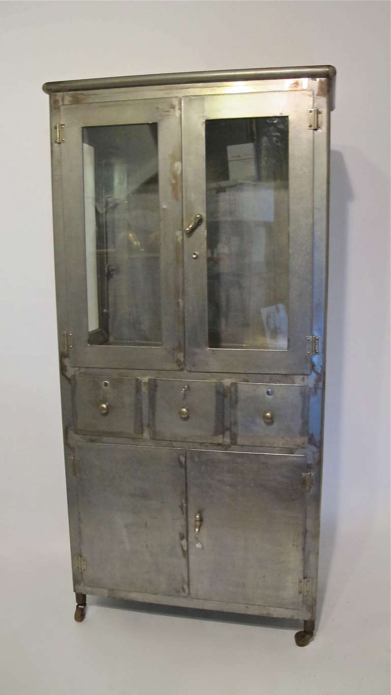 Antique steel medical/apothecary cabinet on original casters. Has two glass shelves in upper section and one metal shelf in lower section.