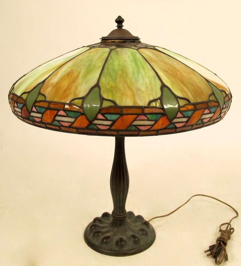 Duffner and Kimberly leaded glass lamp with bronze base. In original condition except for the heat cap. One large glass panel has a hairline crack.