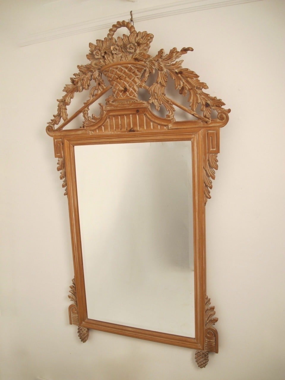 An elaborately hand-carved pine frame with beveled glass mirror and white washed finish. Centre topped by a basket of flowers, scrolling acanthus leaves draping down both sides and flanked by Greek key blocks, ending on pineapple feet. Symbols of