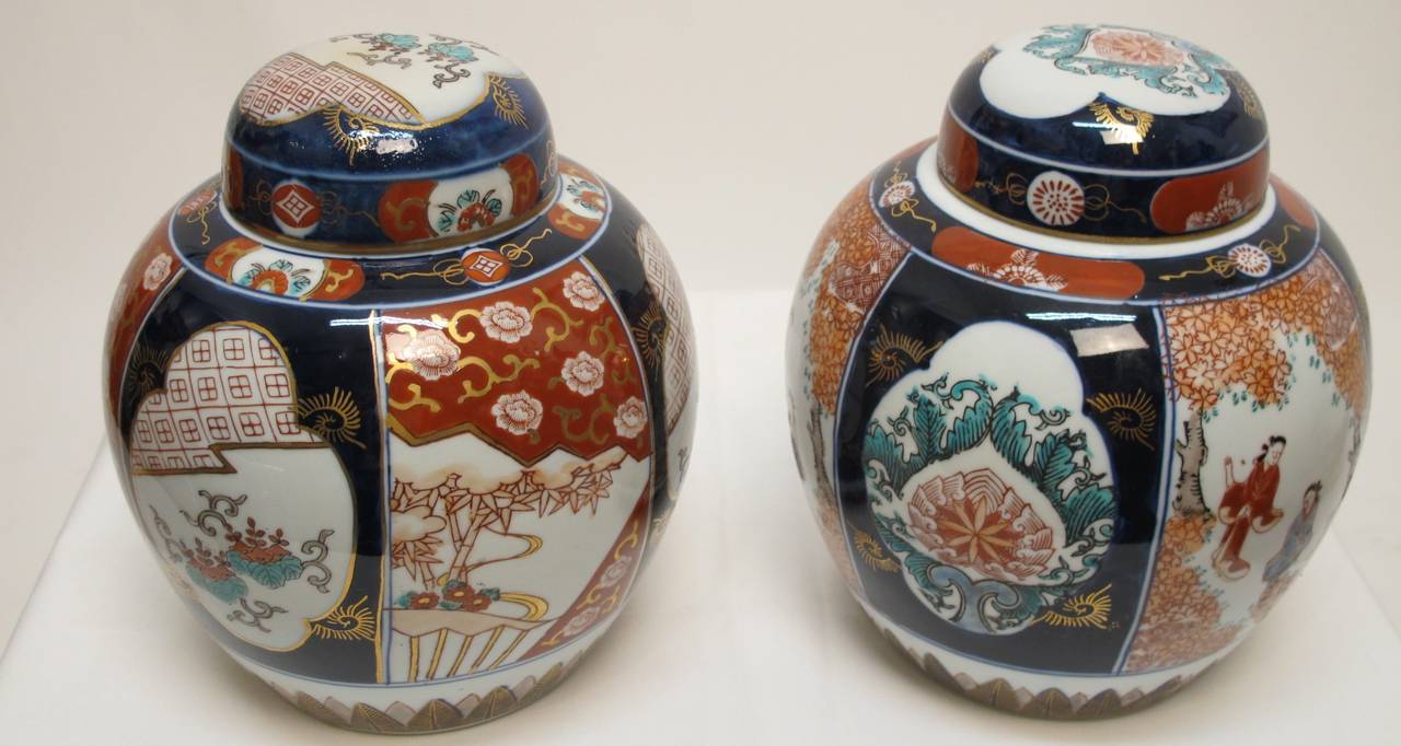 Pair of Japanese Imari covered Ginger Jars, Each painted in the traditional Blue and Iron Red with panels of geometric designs and prunes alternating with flowers or figures in garden setting.  Japanese, circa 1890.
