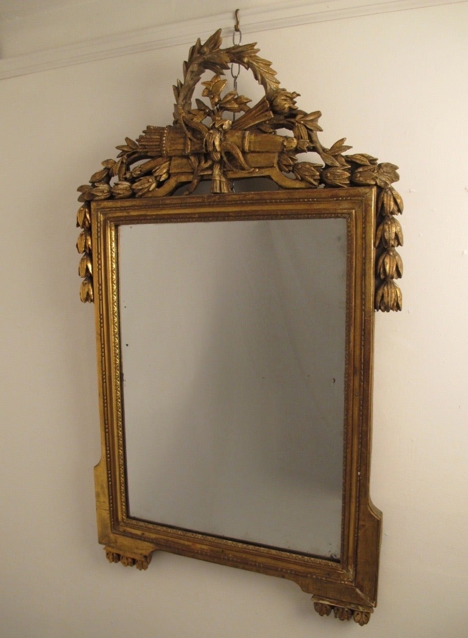 A highly carved and gilt wood frame with laurel leaves, quiver and bell flowers. Has original glass plate mirror, the original gilding is worn and aged in areas, France, circa 1760.