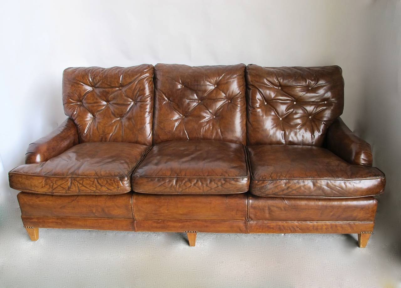 Beautifully aged and worn leather sofa in a deep rich cognac color. Sofa has three cushions with a tufted tight back, and with rolled English arms. Recently reconditioned.