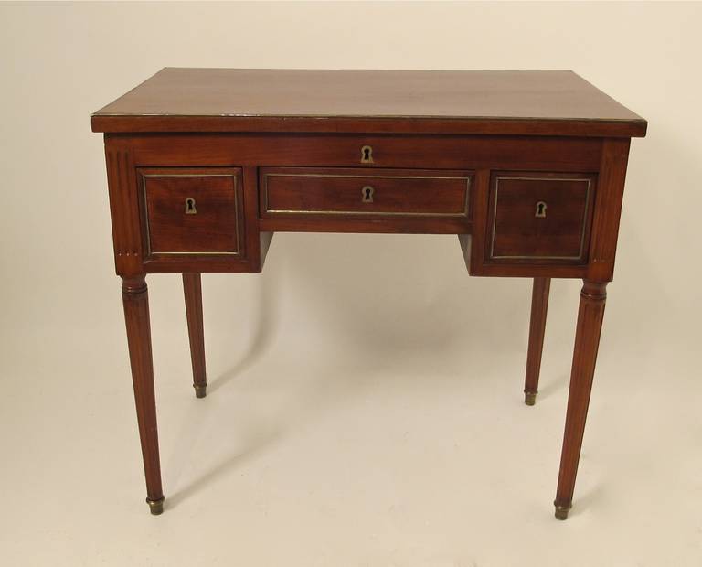 Directoire period solid mahogany and brass-mounted dressing table. Opening to reveal a slightly lowered surface with a mirror mounted on the underside of the lift top. On turned tapering legs having brass capping, France, early 19th century.