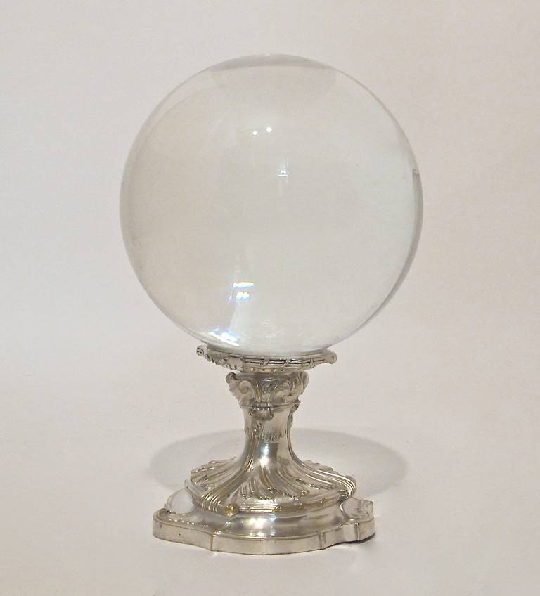 A large clear glass sphere or ball on an antique silver plate stand.