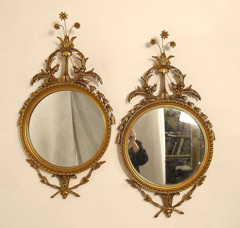 Pair of neoclassical gilt round mirrors with carved leaves and flowers and crossed twigs and leaves at the bottom.
Italian, 20th Century.