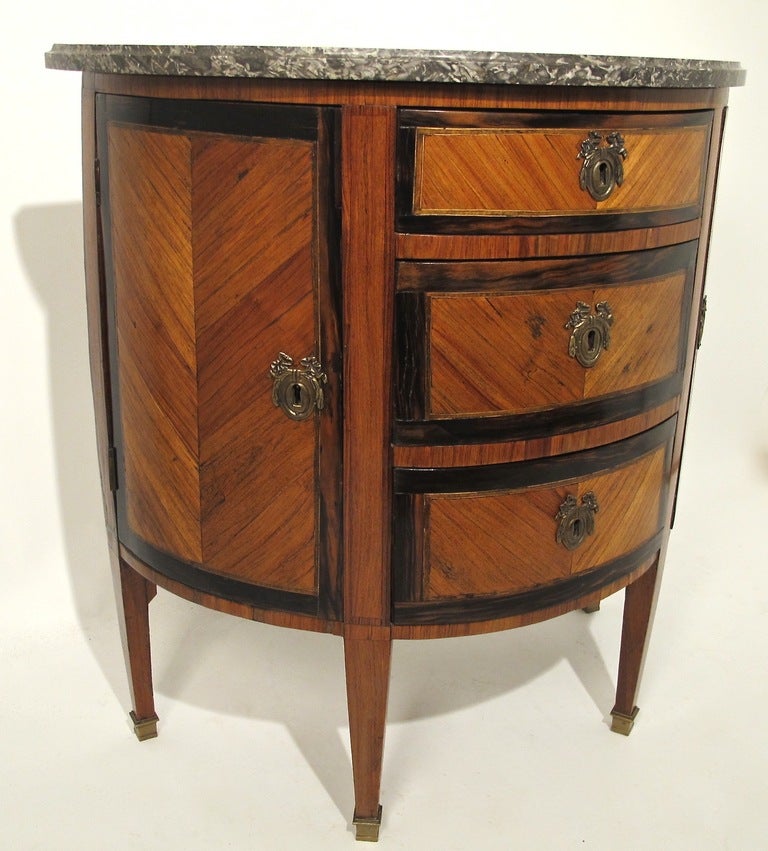 A beautiful rosewood Demi Lune style cabinet. Grey and white marble top, above three drawers and having two side cabinet doors, all standing on tapering legs ending in brass sabots.
Detailed with parquetry inlay of Kingwood and Rosewood.
France,