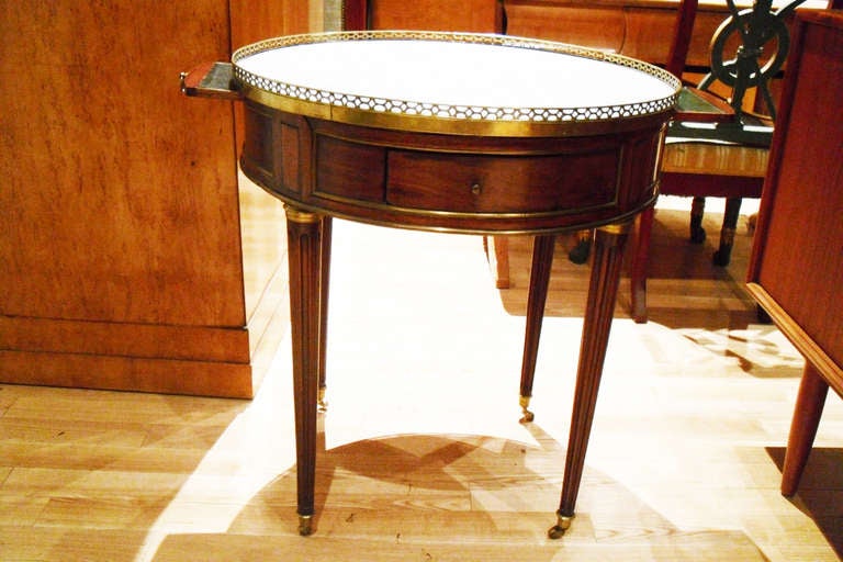 A French Louis XVI Mahogany & Marble top Brass-Mounted Bouillotte Table with two drawers, two candle stands on brass wheels.