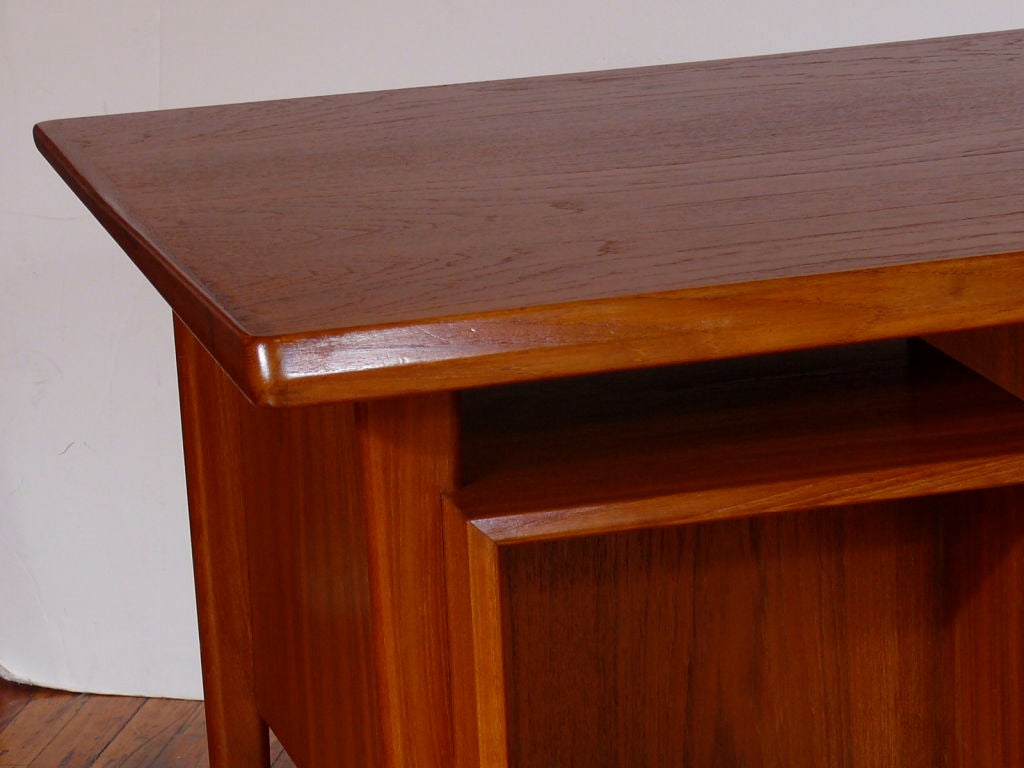 Mid Century Danish Teak Desk with floating top. This desk has a bank of 3 drawers on the left with a lock and a locked file drawer on the right.  The floating top has a tapered gallery around 3 sides.  the front of the desk has bookcases so it can