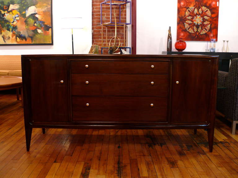 John Stuart Credenza with center drawers and side doors with shelves.  Beautifully finished in natural walnut with brass hardware.
